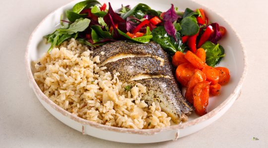 Plato con filete de pescado asado, arroz integral, zanahorias asadas y ensalada de hojas verdes con pimientos rojos